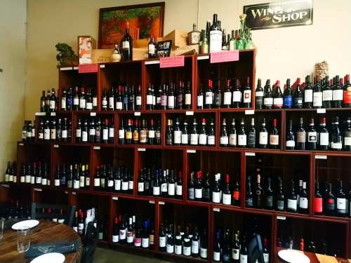 A wall of wooden shelves filled with various wine bottles in a shop, with a sign reading "Wine Shop" above.