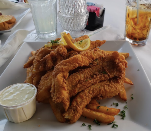 A plate of golden fried fish fillets with fries, garnished with lemon slices and a side of dipping sauce.
