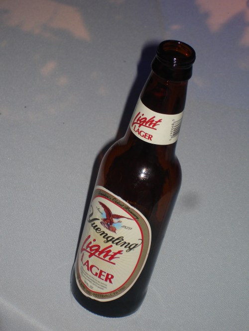 A bottle of Tsingtao Light Lager resting on a table with a soft background.