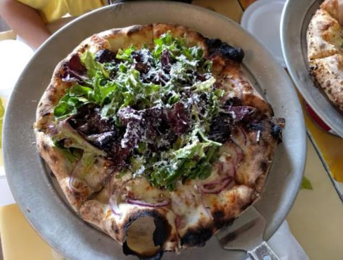 A pizza topped with fresh greens, onions, and grated cheese on a rustic crust, served on a metal tray.