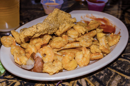 A plate of fried shrimp and fish, served with dipping sauces, on a patterned tablecloth.