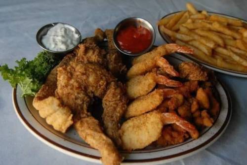 A plate of fried shrimp and chicken, served with fries and dipping sauces on the side.