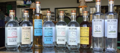 A lineup of various bottles from Big Spring Spirits, including vodka, gin, rum, and whiskey, displayed on a bar.