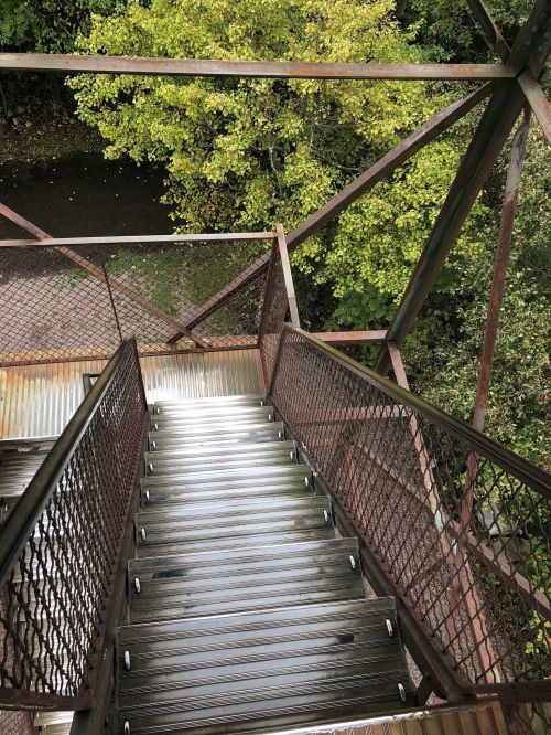 A view from above of metal stairs leading down, surrounded by greenery and trees.