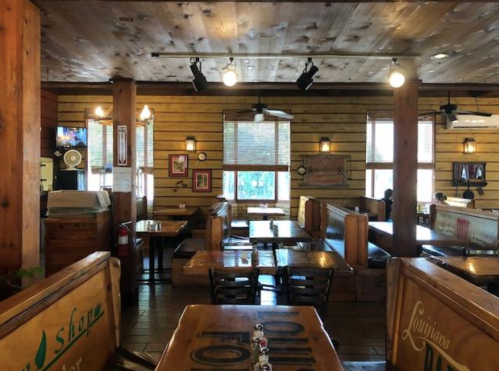 Cozy restaurant interior with wooden decor, tables, and booths, featuring large windows and warm lighting.