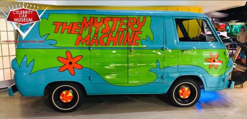 A colorful van with "The Mystery Machine" written on the side, featuring green and blue paint and flower designs.