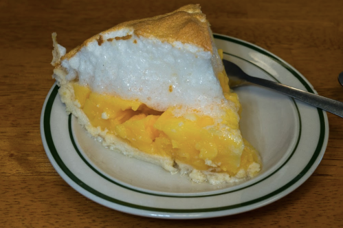 A slice of lemon meringue pie on a plate, featuring a golden filling and a fluffy white meringue topping.