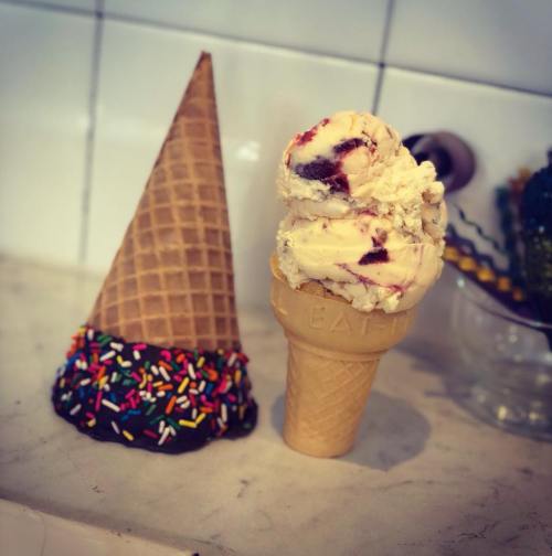 Two ice cream cones: one with colorful sprinkles and chocolate coating, the other topped with creamy ice cream.