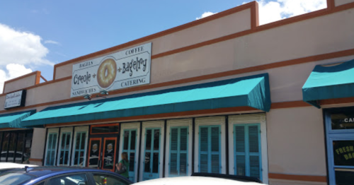 Exterior of a café with teal awnings, featuring a sign that reads "People's Bagelery" and a menu of sandwiches and coffee.