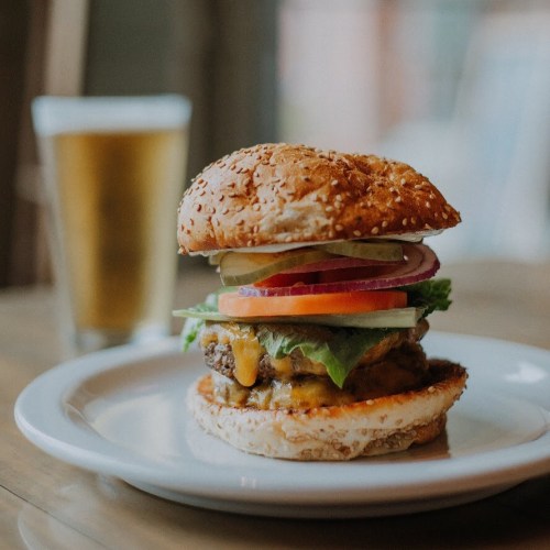A juicy cheeseburger with lettuce, tomato, pickles, and onion on a sesame seed bun, served with a glass of beer.