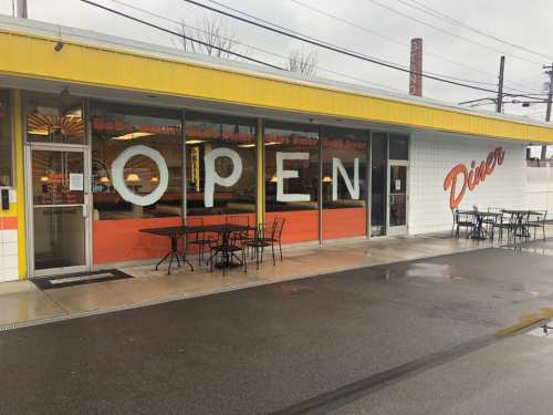 A diner with a bright "OPEN" sign in the window, featuring outdoor seating and a colorful facade.