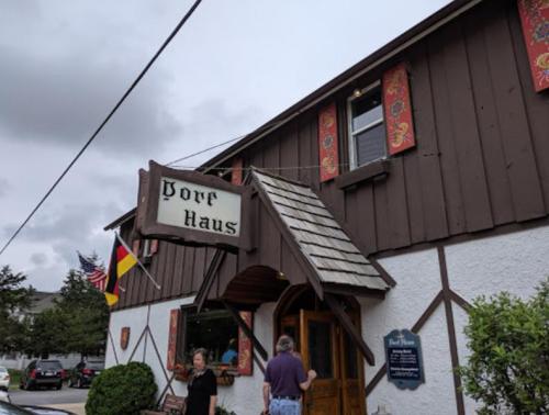 A rustic building with a sign reading "Pork Haus," featuring flags and decorative banners. Two people are entering.