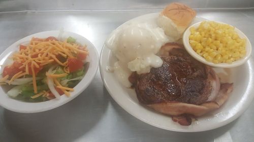 A plate with a grilled pork chop, mashed potatoes with gravy, corn, a biscuit, and a side salad with cheese.