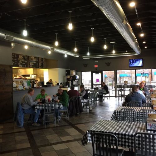 A cozy café interior with checkered tablecloths, patrons dining, and a counter with a menu in the background.