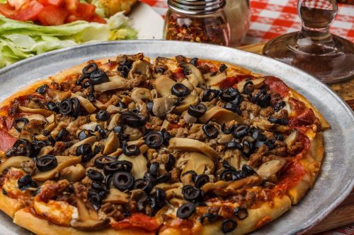 A close-up of a pizza topped with pepperoni, sausage, mushrooms, and black olives on a metal tray.