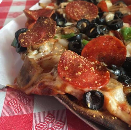 A close-up of a pepperoni pizza topped with olives, green peppers, and spices on a red checkered tablecloth.