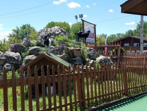 A wooden fence surrounds a grassy area with rocks and two goats on top, near a sign for a rustic lodge.