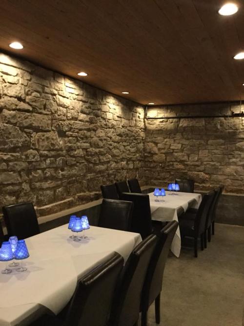 Cozy restaurant interior with stone walls, wooden ceiling, and tables set with blue candle holders.