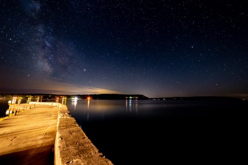 A serene night scene of a calm lake under a starry sky, with a wooden pier extending into the water.