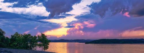 A serene sunset over a lake, with colorful clouds reflecting on the water and trees lining the shore.