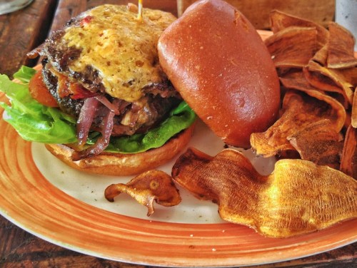 A juicy burger with melted cheese, lettuce, and onions, served with crispy sweet potato chips on the side.