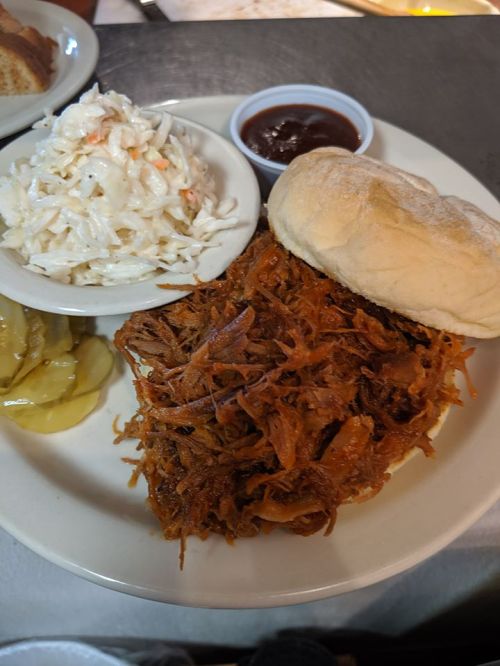 A plate featuring pulled pork, coleslaw, a biscuit, and a side of baked apples with barbecue sauce.