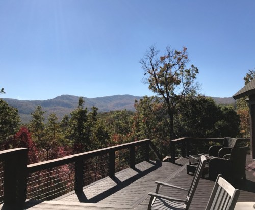 A scenic view from a deck overlooking mountains and trees under a clear blue sky.