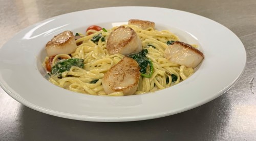 A plate of pasta with sautéed spinach, cherry tomatoes, and seared scallops in a creamy sauce.