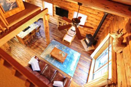 Cozy wooden cabin interior with a living area, ceiling fan, and a view of a rustic kitchen and decorative elements.