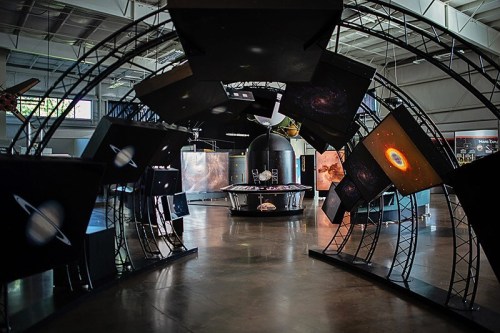 A futuristic exhibit featuring screens displaying galaxies and planets, set in a spacious, well-lit museum environment.