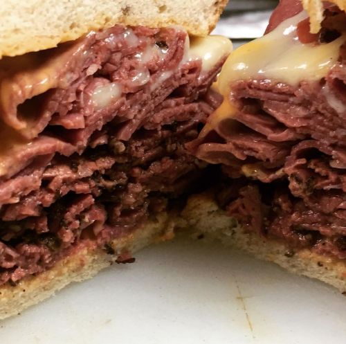 Close-up of a sandwich filled with layers of sliced meat and melted cheese between two slices of bread.