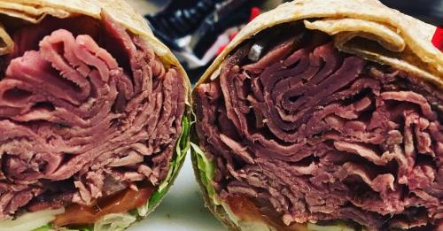 Close-up of a sliced wrap showing layers of roast beef, lettuce, and tomato inside a tortilla.