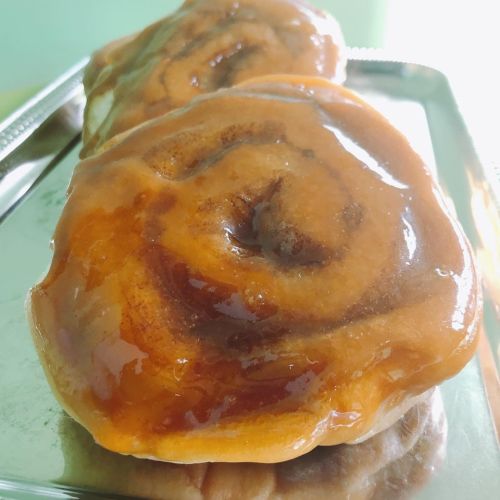 Two glossy, freshly baked cinnamon rolls on a silver tray, showcasing their swirled layers and sticky glaze.