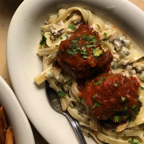 A bowl of fettuccine pasta topped with meatballs and marinara sauce, garnished with fresh parsley.