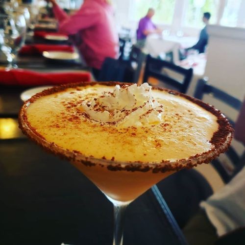 A close-up of a creamy cocktail topped with whipped cream and a sprinkle of cinnamon, served in a glass.
