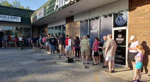 A long line of people waiting outside a barbecue restaurant on a sunny day.