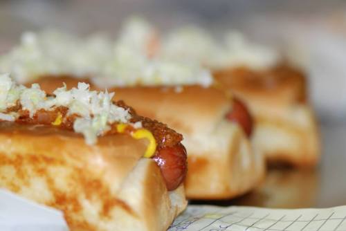Three hot dogs topped with chili, mustard, and chopped onions on a soft bun, arranged in a row.