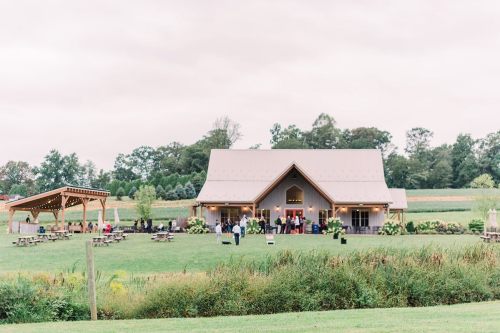A rustic barn venue surrounded by greenery, with people gathered outside for an event.