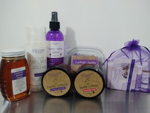 A collection of lavender-themed products, including honey, creams, a linen spray, and sachets, arranged on a surface.