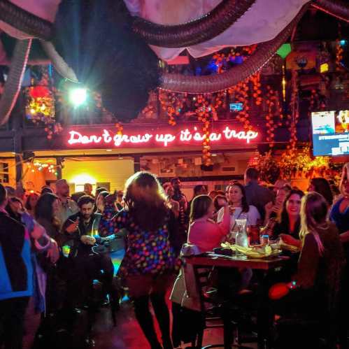 A lively bar scene with colorful decorations and a performer in a polka dot outfit, under a neon sign reading "Don't grow up it's a trap."