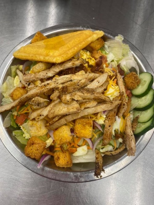 A bowl of salad topped with grilled chicken, croutons, cheese, cucumbers, and a fried plantain.
