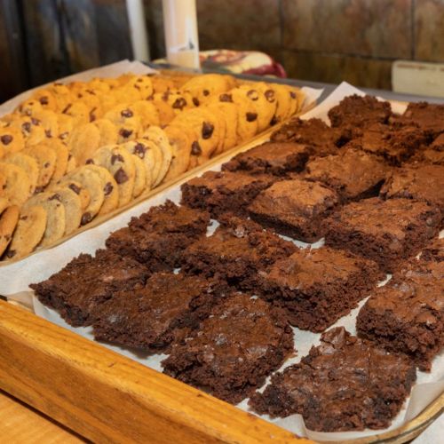 A wooden tray filled with chocolate chip cookies and rich, fudgy brownies on parchment paper.