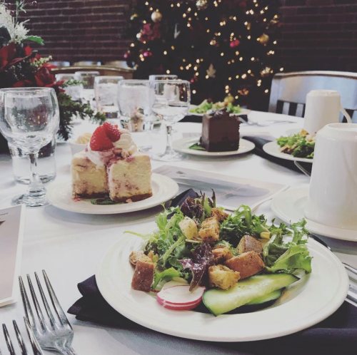 A festive table setting with a salad, dessert, and drinks, decorated for the holidays with a Christmas tree in the background.