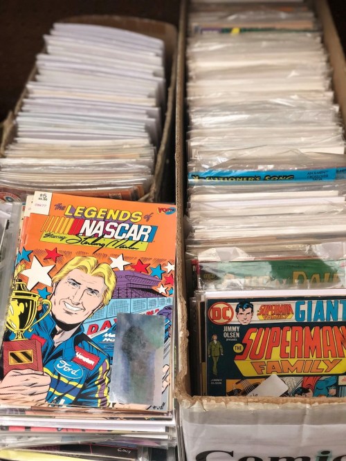 Two boxes filled with comic books, featuring a NASCAR comic on top of one stack and various titles in the other.