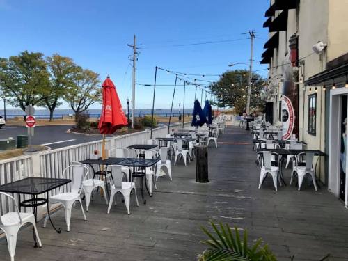 Outdoor dining area with empty tables, umbrellas, and a view of the water under a clear blue sky.