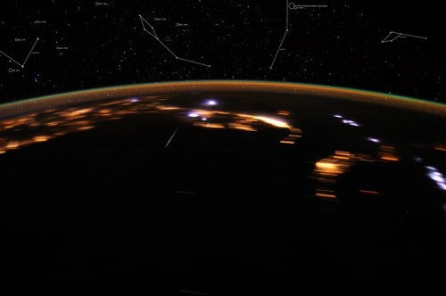 A view of Earth from space, showcasing city lights and constellations against a starry background.
