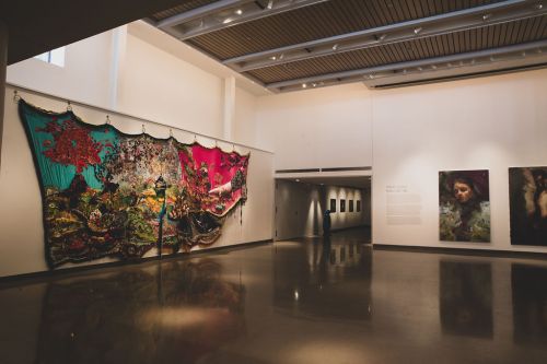 A vibrant art installation with colorful fabric and paintings displayed in a well-lit gallery space.