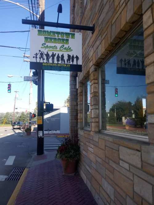Sign for "Hometown Heroes Sports Cafe" on a stone building, with a view of the street and traffic lights nearby.