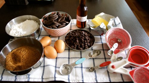 Ingredients for baking: flour, sugar, eggs, chocolate chips, cookies, and vanilla extract on a checkered cloth.