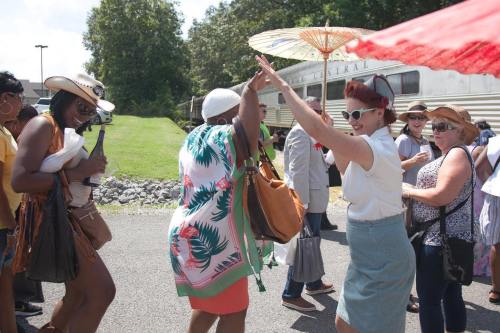 A lively outdoor scene with people dancing and enjoying a sunny day, some holding umbrellas and wearing summer attire.
